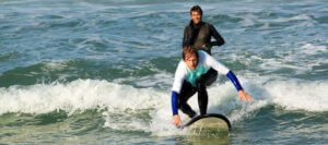 Surfer and surf teacher on atlantic coast surf lesson in portugal, wave, surfer rides wave, teacher provides assistance, sunshine