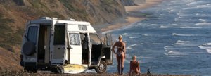 surfer girls watch sunset at atlantic coast by the campervan