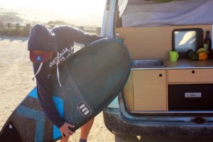 Boy holds surfboard next to campervan in surf holidays