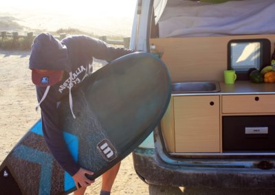 Boy holds surfboard next to campervan in surf holidays
