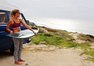 Girl with surfboard next to campervan