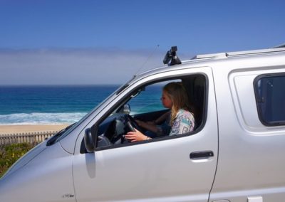 Woman driving Atlantic Coast Campers van along Portugal's coastline, surf adventures await