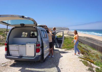 A group of young tourists enjoying the view of the Atlantic Coast from their Atlantic Coast Campers' Ginginha campervan, ideal for surf and travel adventures in Portugal.
