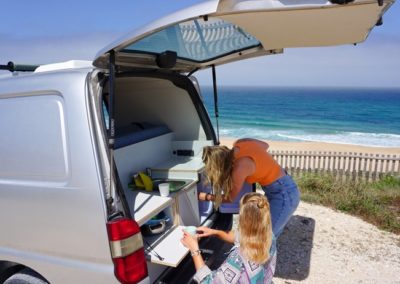 Two people preparing food in the back of a Ginginha campervan by Atlantic Coast Campers on the coast of Portugal, ideal for surf enthusiasts and travel lovers.